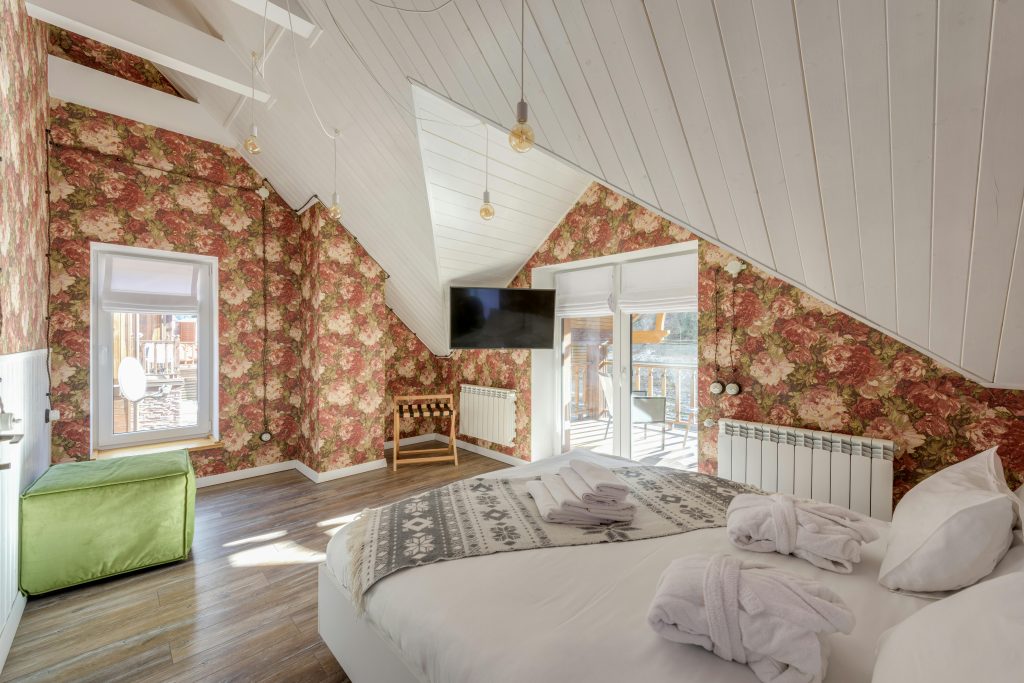 Spacious attic bedroom featuring floral wallpaper, cozy bed, and balcony view.